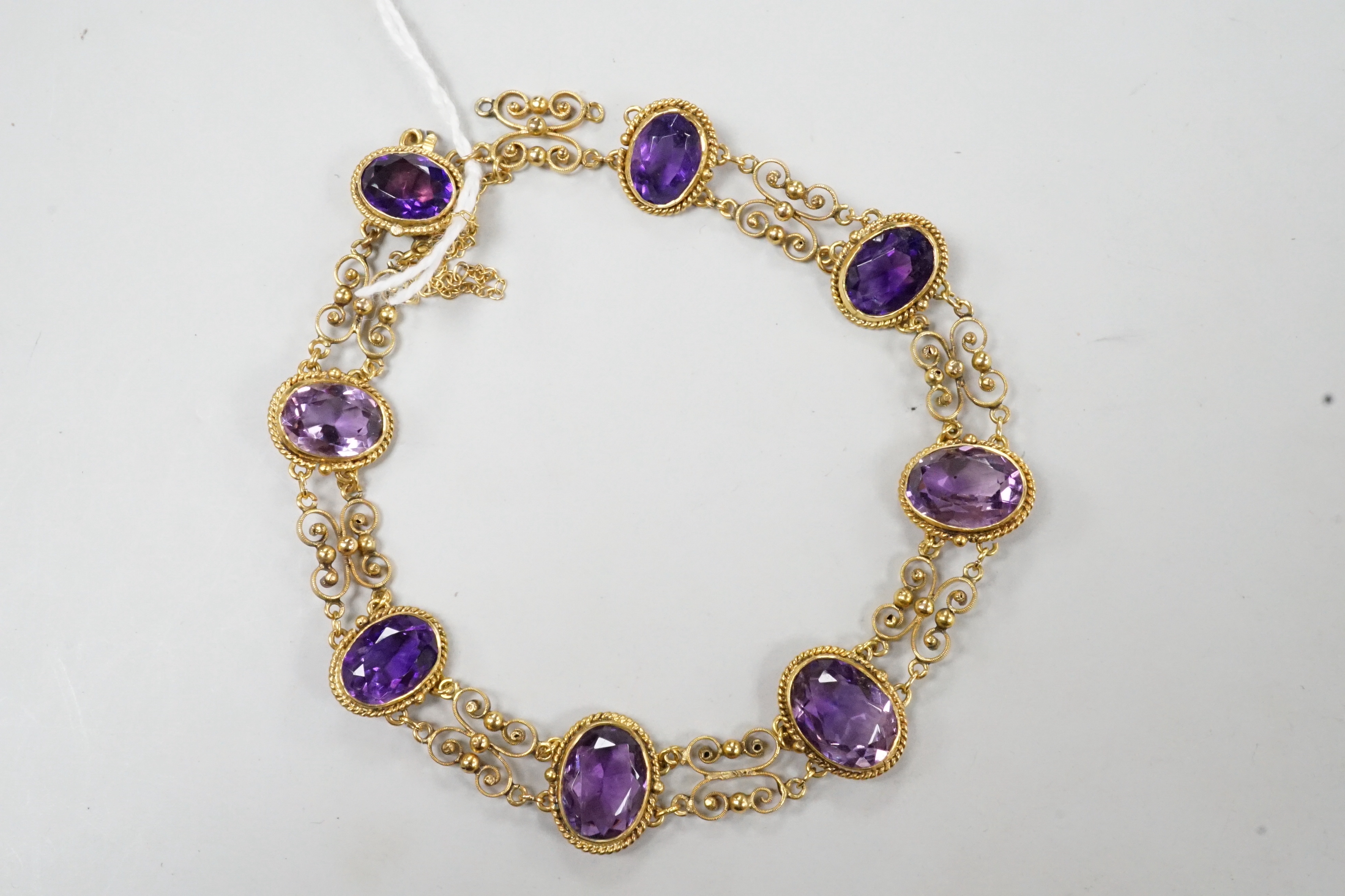 A late Victorian yellow metal and eight stone oval cut amethyst set fancy link bracelet, 18cm, gross weight 9.6 grams.